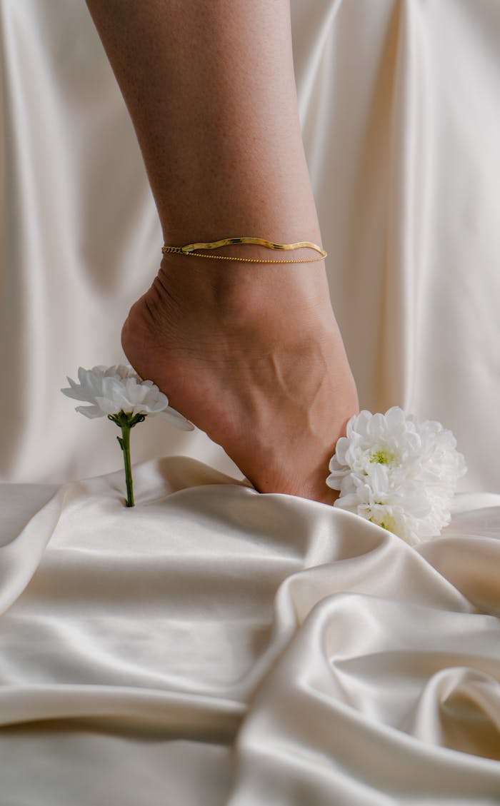 Crafting Captivating Headlines: Your awesome post title goes here A graceful foot with gold anklet on luxurious silk, surrounded by white flowers.