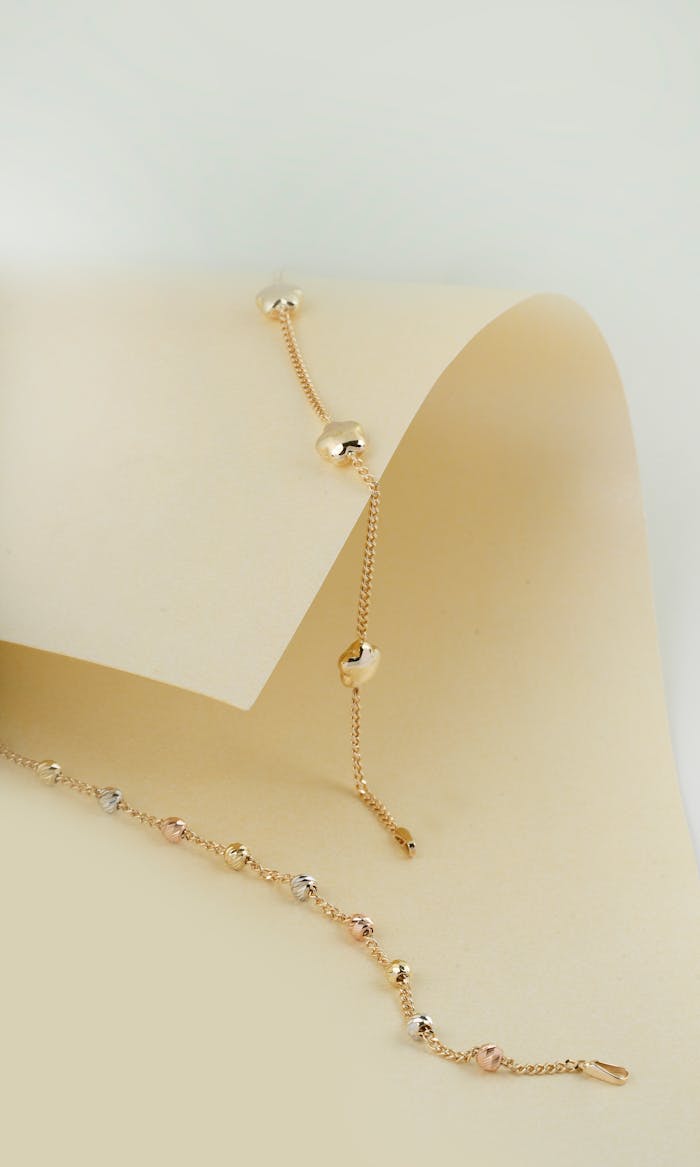 Delicate gold chain with beads on a minimalist cream backdrop, perfect for jewelry showcasing.