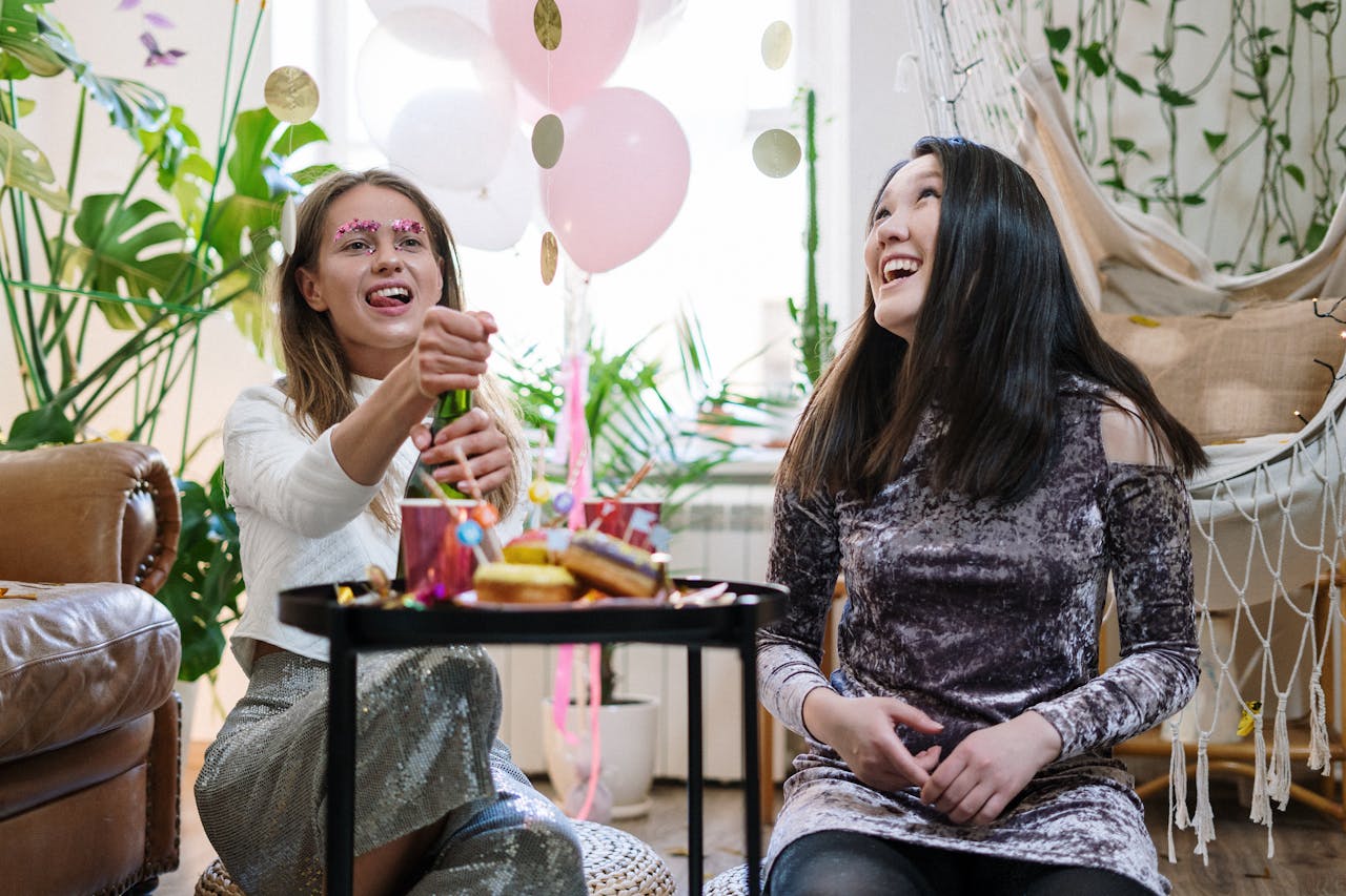 Women celebrating indoors with balloons and snacks, sharing laughter and happiness.